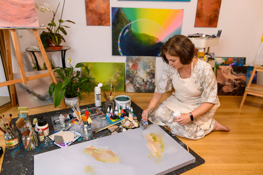 Mona Barbu painting on the studio floor, surrounded by brushes, inks and finished canvases